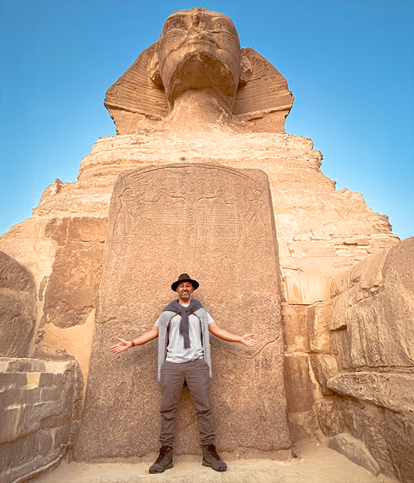 A figure with arms outstretched before a monumental carved sphinx
