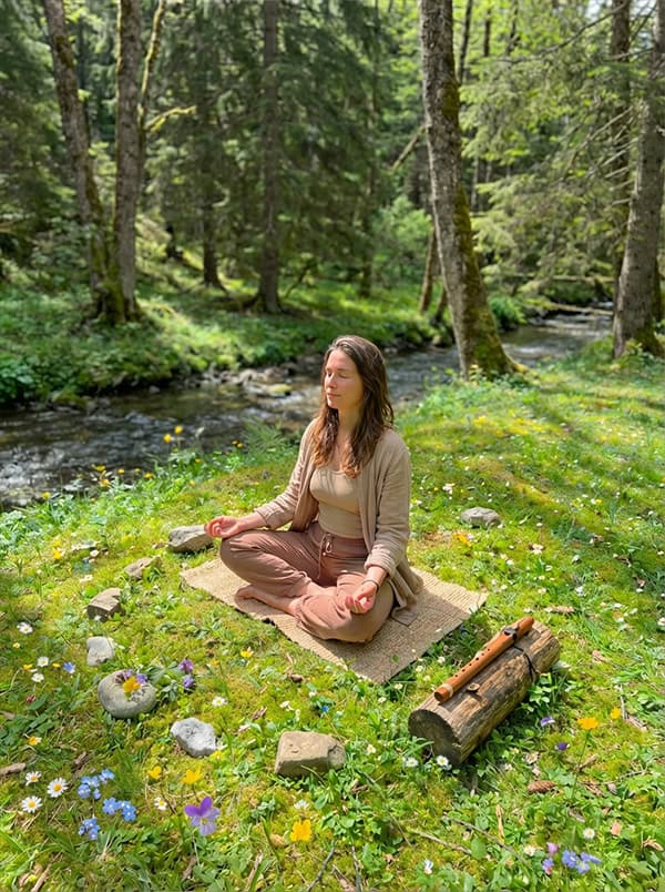 A woman meditating in a sunlit forest clearing