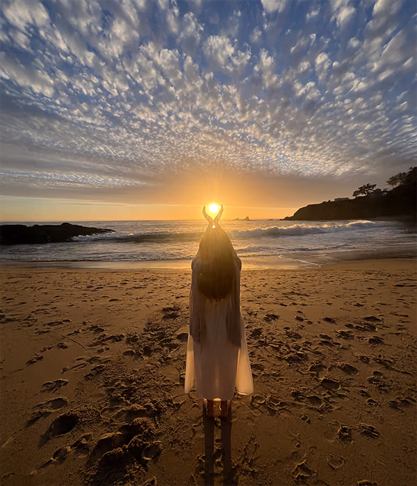 A figure on a beach at sunset holding a point of light